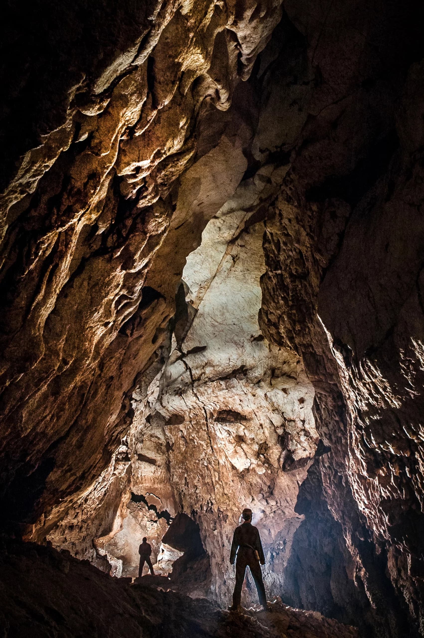 Espeleólogos explorando el interior de una gran cueva iluminada con frontales